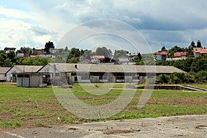 Elongated dilapidated military hangars with broken windows and destroyed walls surrounded with grass and family houses