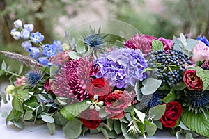 Elongated floral arrangement in vintage metal vase. table setting. Blue and red color. Gorgeous bouquet of different