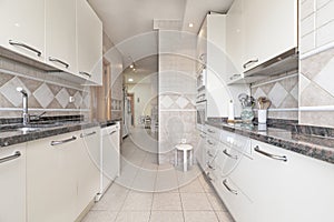 elongated kitchen with cabinets on each side of the walls, simil granite countertops, white cabinets with yellow pulls