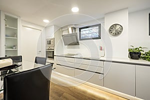 Elongated modern conventional kitchen with handleless cabinets with many large drawers and a glass top table with black