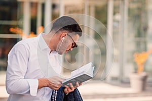 An eloquent businessman is outside, he is enjoying in the beautiful weather while looking at the notebook. Urban businessman on
