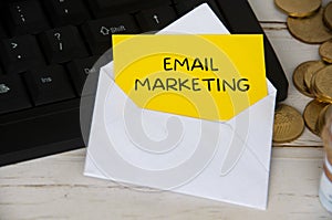 Email marketing text on yellow notepad in an envelope on keyboard computer with gold coins.