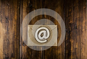 An email sign on a craft envelope lies on a vintage wooden table. Concept e-mail message letter