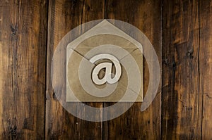 An email sign on a craft envelope lies on a vintage wooden table. Concept e-mail message letter