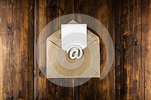 An email sign with white blank paper on a craft envelope lies on a vintage wooden table. Concept e-mail message letter. Top view