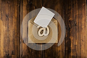 An email sign with white blank paper on a craft envelope lies on a vintage wooden table. Concept e-mail message letter. Top view