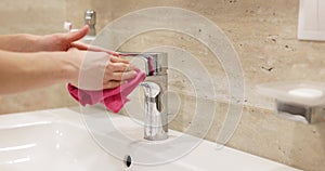 emale hand with pink rag washes faucet in white sink