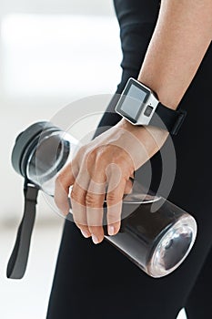 emale hand with smartwatch holding reusable bottle with water.