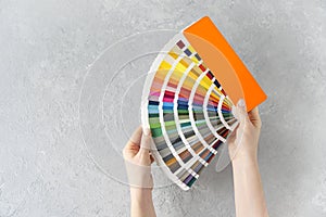Emale hands holding a ral colors palette fan on a concrete background.