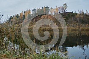 Embankment mountain with yellow-green forest reflected in water as if in mirror. Nature of Moscow region in autumn