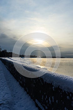 Embankment in winter. Dawn on the river. Winter river in the city. City embankment by the river on a sunny winter day with snow.