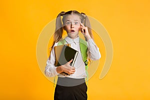 Embarassed Elementary Student Looking At Camera Holding Books On Yellow Background