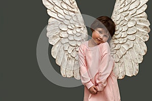 An embarrassed angel on a gray asparagus background.  Cute little girl in pink dress with angel wings. Copy space