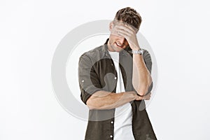 Embarrassed and awkward handsome ex-boyfriend trying hide behind hand as making facepalm gesture so girl would not