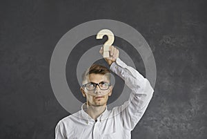 Embarrassed businessman with emotion of doubt on his face holding wooden question mark over his head