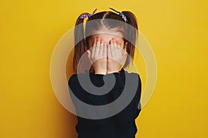 Embarrassed shy cute girl with ponytails covering her face with both hands photo