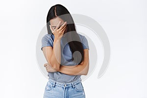 Embarrassed and tired, pissed young asian woman making facepalm, lean on arm and close eyes, sighing fed up, bothered by