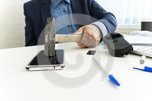 embittered businessman hits a smartphone with a hammer in workplace. Unsuccessful business negotiations concept. failure