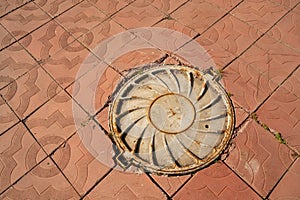 Embossed cast-iron cover of the manhole - part of the manhole cover is located on the pavement made of concrete slabs