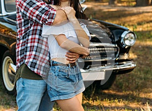 embrace.Love and affection between a young couple at the park, near the old car. a guy in a plaid plane and jeans, a girl in short