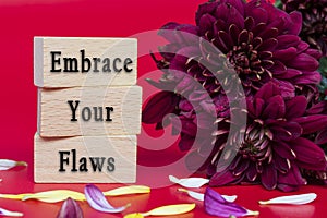 Embrace your flaws text on wooden cube and with flowers bouquet background.