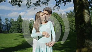 Embraced pregnant couple enjoying pregnancy in a beautiful park on a sunny day