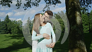 Embraced pregnant couple having intimate moment in a beautiful sunlit garden