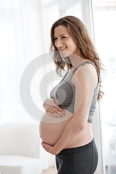Embracing her maternal instincts. a young pregnant woman standing in her home.