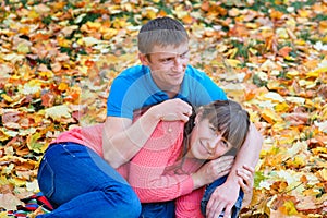 Embracing young couple sitting in a park on yellow leaves in aut