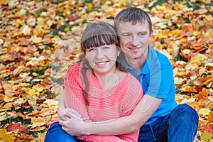 Embracing young couple sitting in a park on yellow leaves in aut