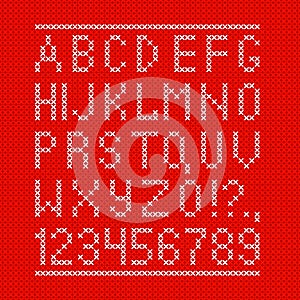 Embroided by cross stitch english alphabet with numbers and symbols on red cloth texture.