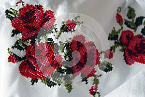Embroidery with beautiful colorful red roses and green leaves, closeup. Cross-stitch texture, folk costume