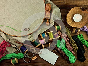 Embroidery needlework background with linen in hoop. Colorful floss thread, scissors, card tag in female hand. Handmade