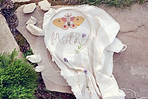 Embroidery project - butterfly on linen cloth in a hoop with a word Moth, made of thread and a few lavender flowers on it.