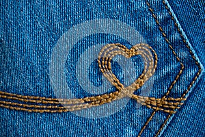 Embroidery in the shape of a heart on a denim pockets. Blue denim background with brown stitch