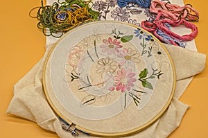 Embroidery tools on cotton fabric with hoop, sketch, needle and colored threads on orange background