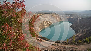 Emerald Azure lake in a flooded quarry in the shape of a heart and autumn red foliage. Oval lake in mining industrial