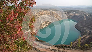 Emerald Azure lake in a flooded quarry in the shape of a heart and autumn red foliage. Oval lake in mining industrial