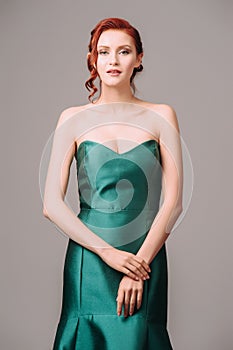 Emerald ball gown. Young lady in long green evening dress. Ginger woman posing in studio. Beautiful model