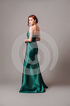Emerald ball gown. Young lady in long green evening dress. Ginger woman posing in studio