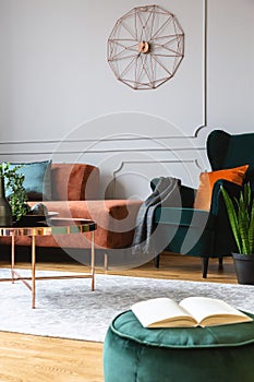 emerald green armchair with orange pillow next to corner sofa and coffee table