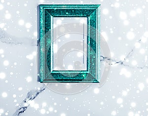 Emerald green photo frame and glowing glitter snow on marble flatlay background for Christmas and winter holidays