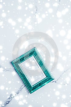 Emerald green photo frame and glowing glitter snow on marble flatlay background for Christmas and winter holidays