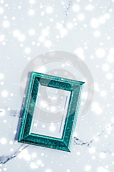 Emerald green photo frame and glowing glitter snow on marble flatlay background for Christmas and winter holidays