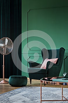 Emerald green velvet armchair with pastel pillow in trendy living room interior with copper accents