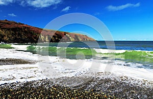 Emerald green waves crashing onto a pebble beach