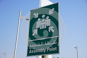 Emergency assembly point information sign in white paint on green background fixed to a pole to direct people where to go in case