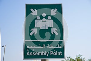 Emergency assembly point information sign in white paint on green background fixed to a pole to direct people where to go in case