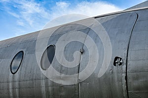 Emergency exit doors and windows of an old commercial airplane showing silver metal surfaces and parts on a blue sky background