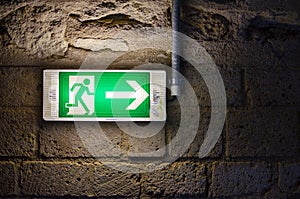 Emergency exit light green sign on brick wall in the dark